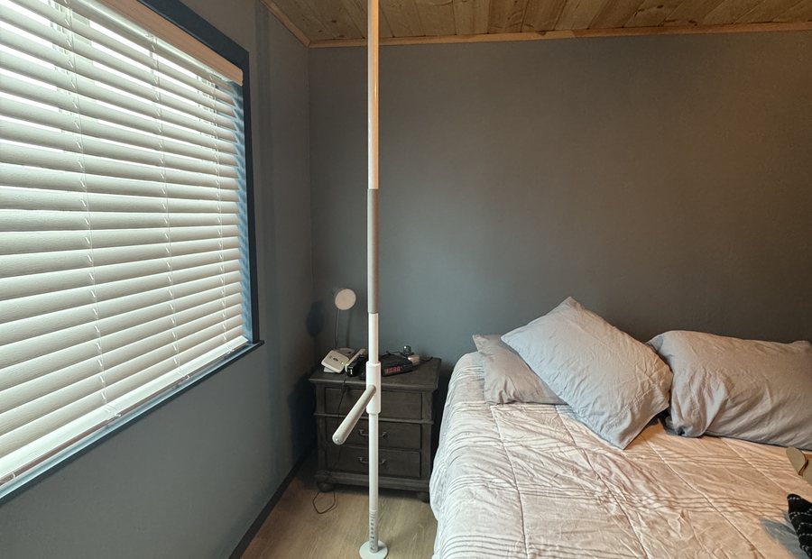Floor-to-ceiling transfer pole with a swing-out handle beside a bed