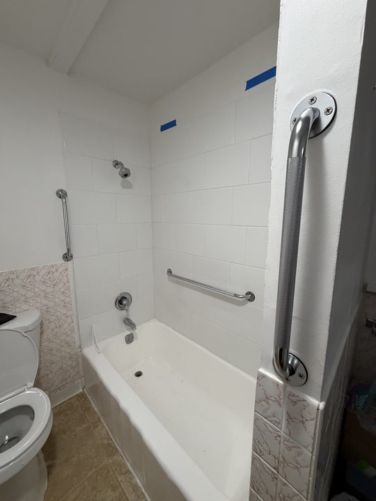 After: tiled bathtub with three chrome grab bars